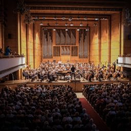 A packed concert venue with a symphony orchestra playing.
