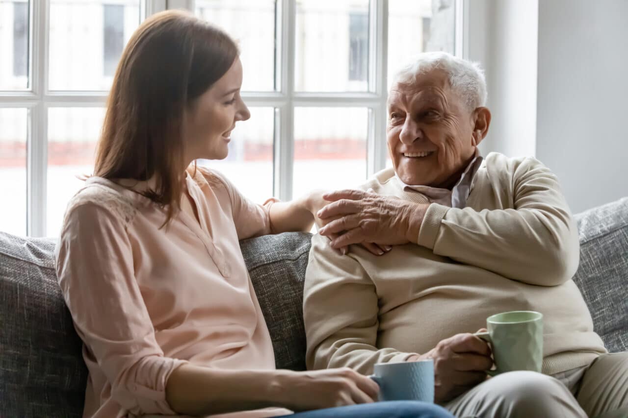 Young adult woman talking with her older father on the couch.