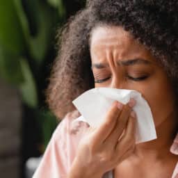 Sneezing coughing ill young african woman using paper napkin, having runny nose, blowing her nose. Coronavirus, infectious disease, flu, cold.