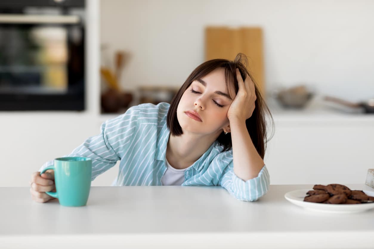 Tired woman leaning on counter, holding mug.