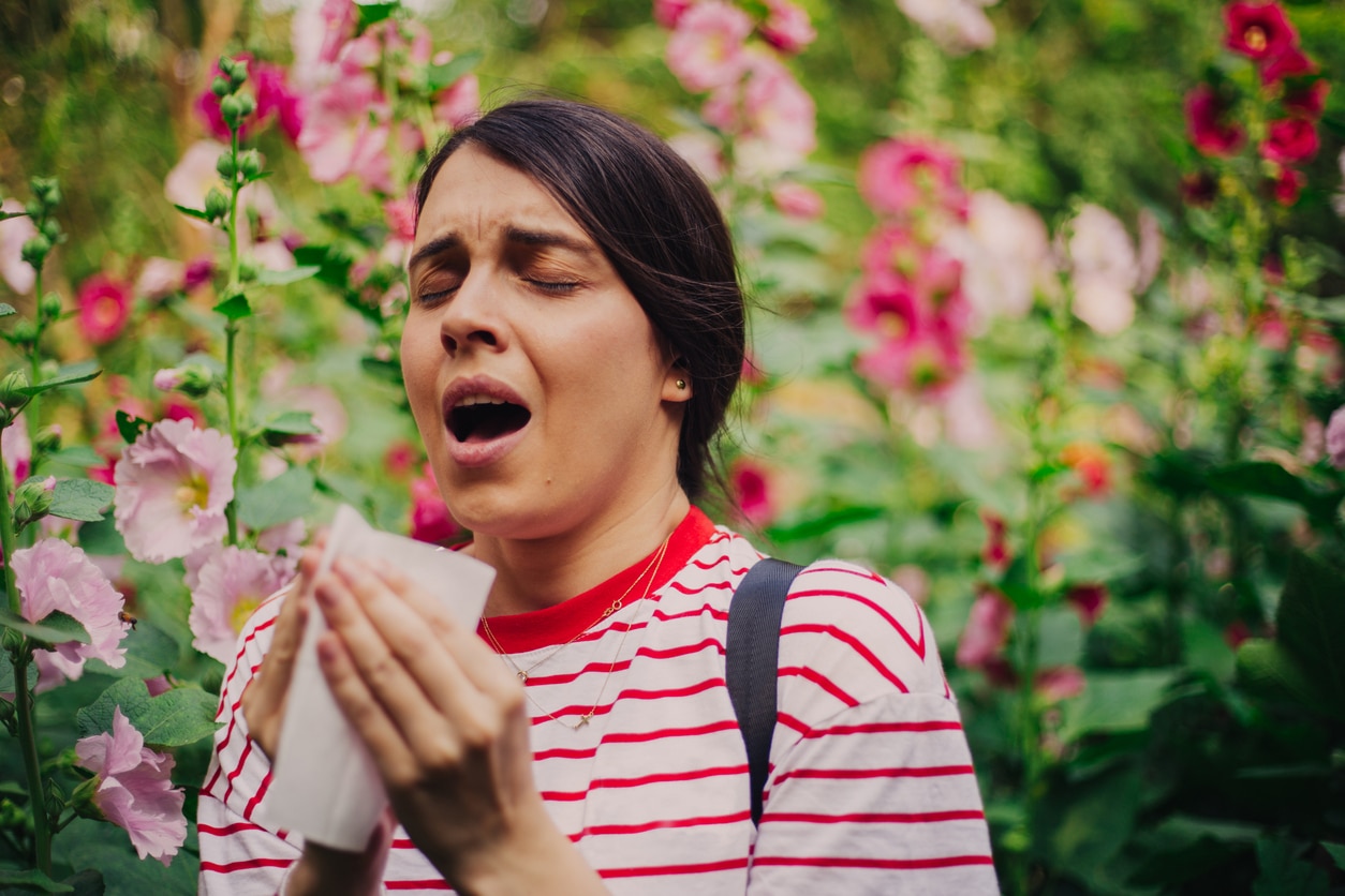 Woman sitting in a garden sneezing into a tissue.
