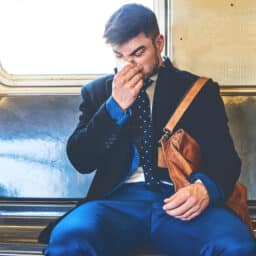 Man suffering from allergies blows his nose on a train.