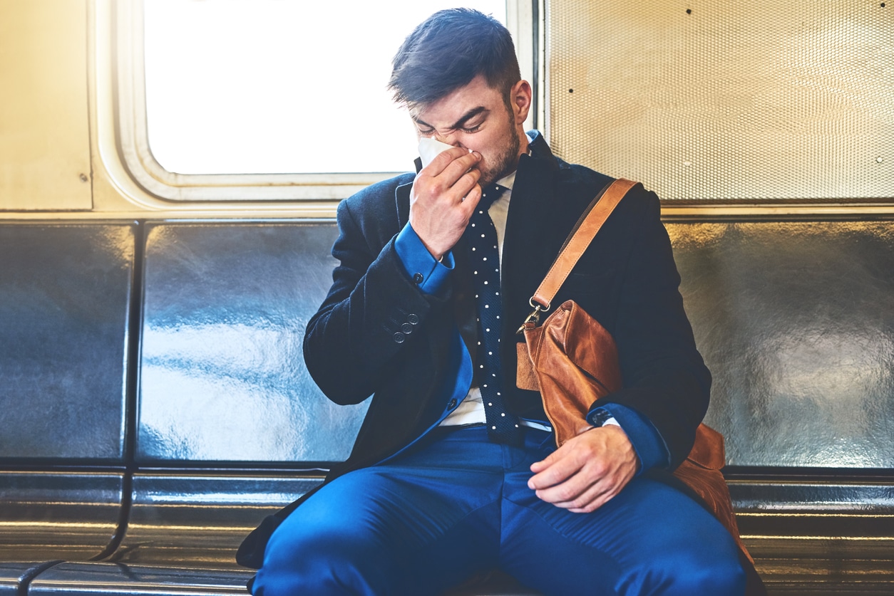 Man suffering from allergies blows his nose on a train.