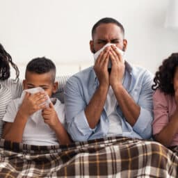 A family of four all blowing their noses into tissues.