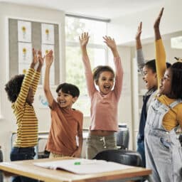 Happy kids in the classroom raising their hands and cheering.