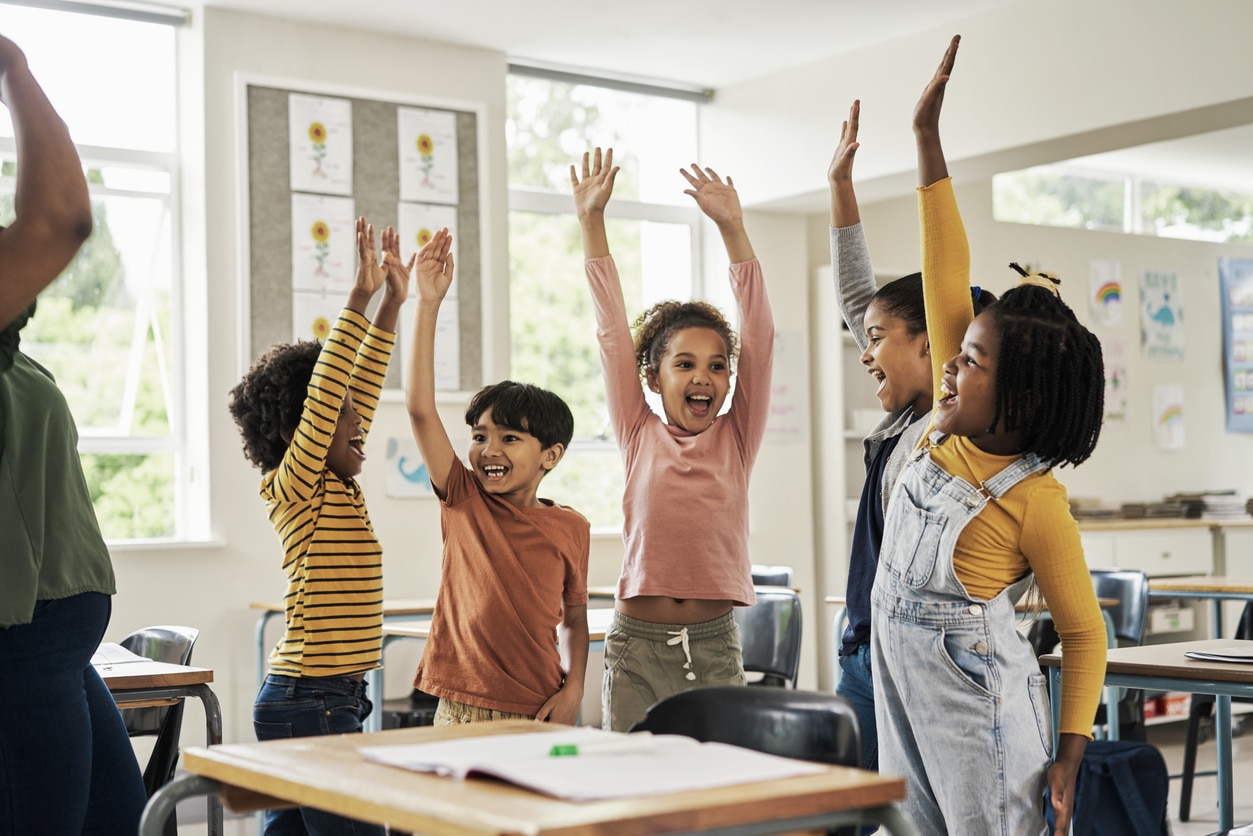 Happy kids in the classroom raising their hands and cheering.