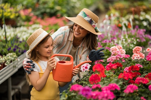Little girl helping her mother water the plants at a nursery.