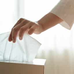 Close-up of a hand reaching for a tissue from a tissue box.