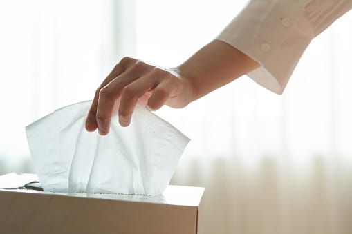 Close-up of a hand reaching for a tissue from a tissue box.