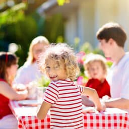 Close-up of a smiling kid at an outdoor picnic with their family.