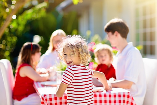 Close-up of a smiling kid at an outdoor picnic with their family.