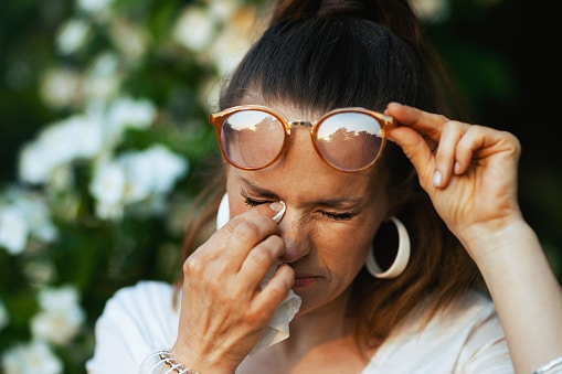 Woman struggles with watery eyes, a common summer allergy symptom. She wipes her eyes with a handkerchief.