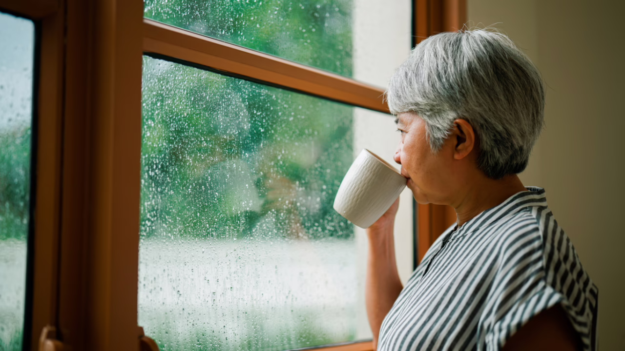 Contented woman sips a cup of coffee and stares out the window at the rainy weather.